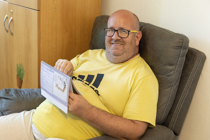 Pan Jiří sedí v&nbsp;pohodlném křesle a&nbsp;listuje kalendářem, zatímco se usmívá do objektivu.